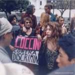 Fotografía histórica de activistas de Coccinelle en una acción pública; una participante sostiene un cartel contra la discriminación.